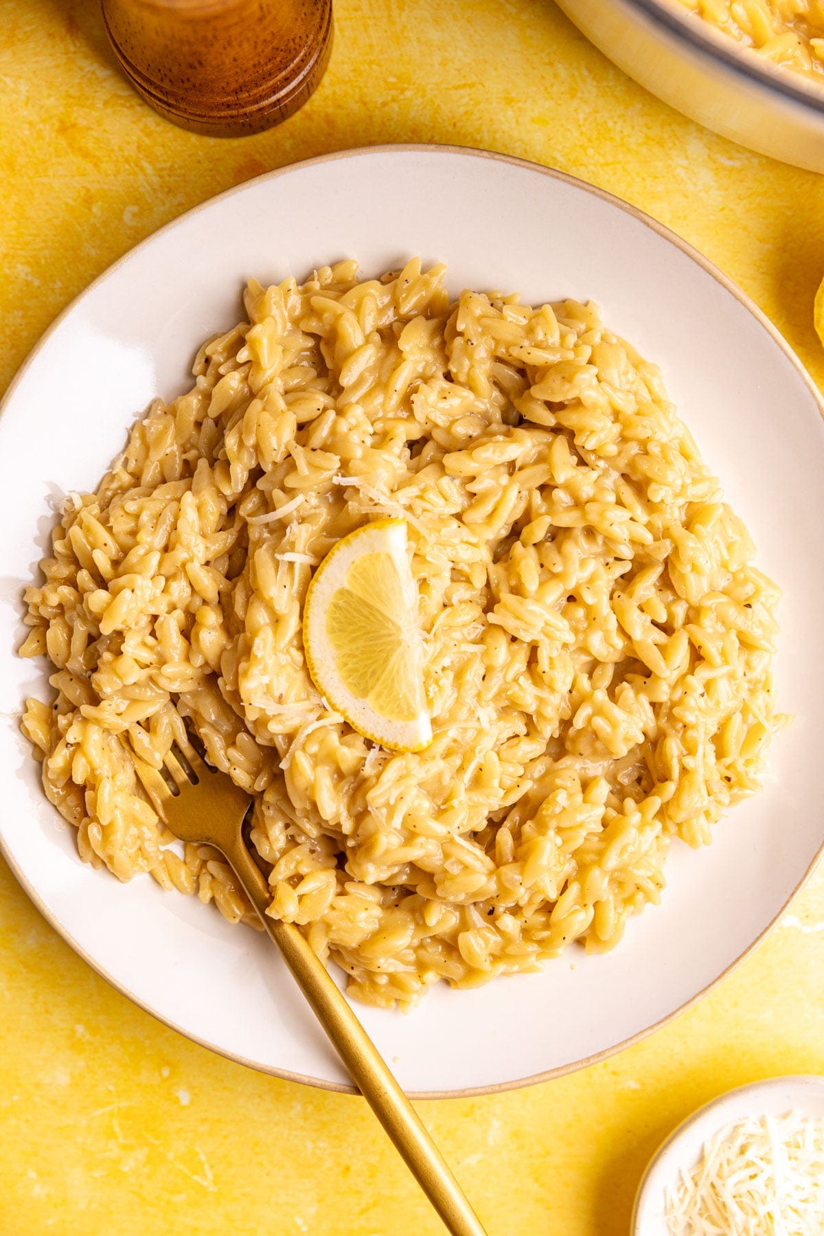 A plate of creamy lemon orzo, garnished with lemon slices and vegan parm.