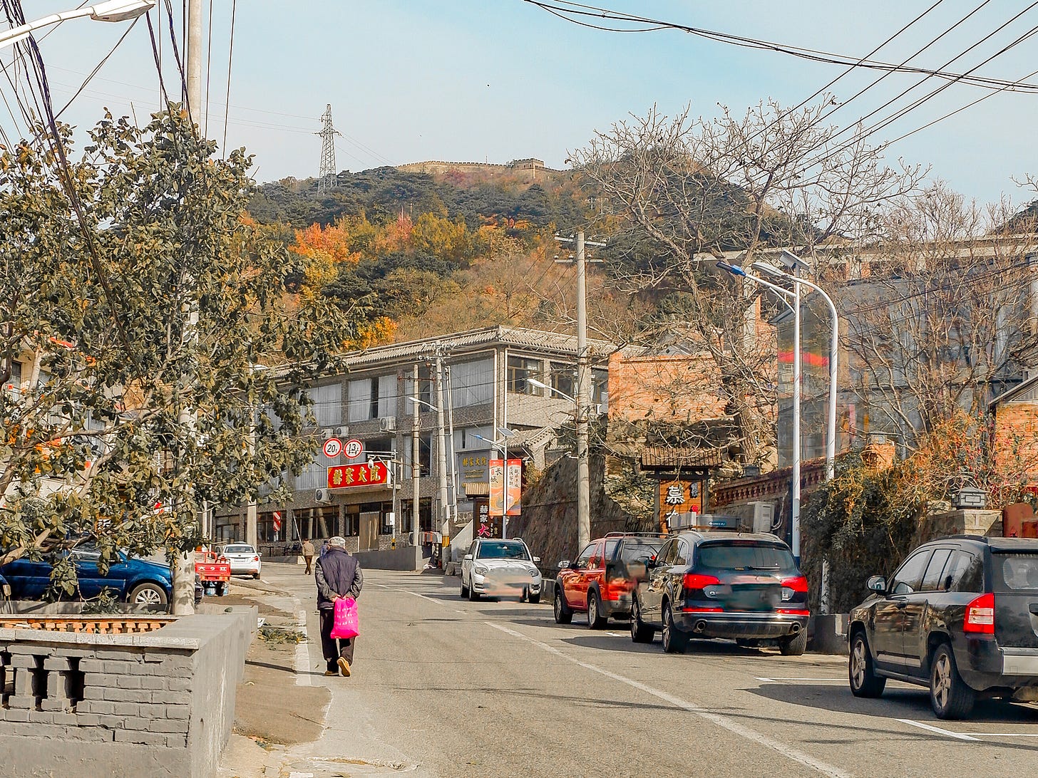 A local resident ambles up the asphalt carrying a bright plastic bag, completely unbothered by the ancient watchtowers guarding the mountain spine directly behind him.