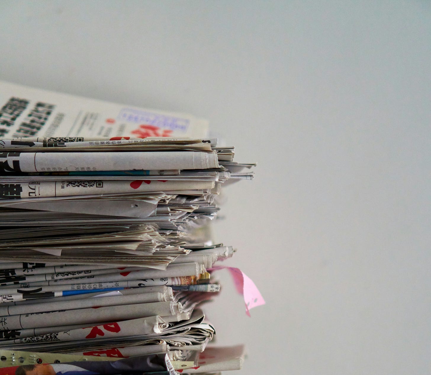a stack of many newspapers, lying flat on top of each other, against a white wall background a stack of many newspapers, lying flat on top of each other, against a white wall background