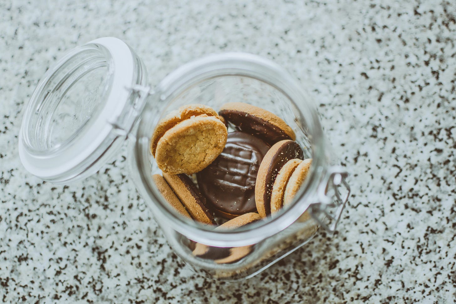 a glass jar of chocolate-coated cookies, open on a grey granite surface