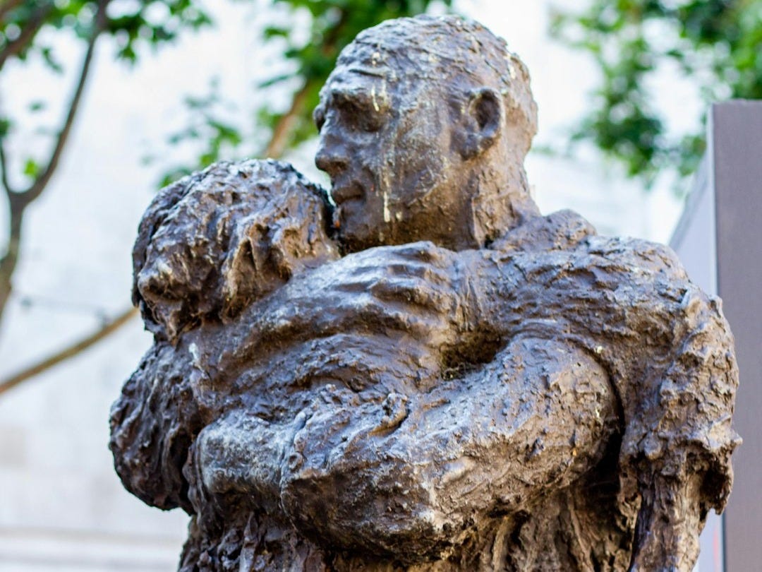 A bronze sculpture depicts a man hugging a child. A bronze sculpture depicts a man hugging a child.