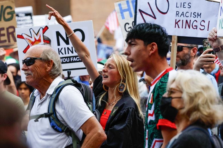 Nova Berger, 21, participates in a “No Kings” protest against President Donald Trump at the University of Washington on Saturday in Seattle. Berger is wearing a graduation gown to walk at commencement this afternoon. (Jennifer Buchanan / The Seattle Times)