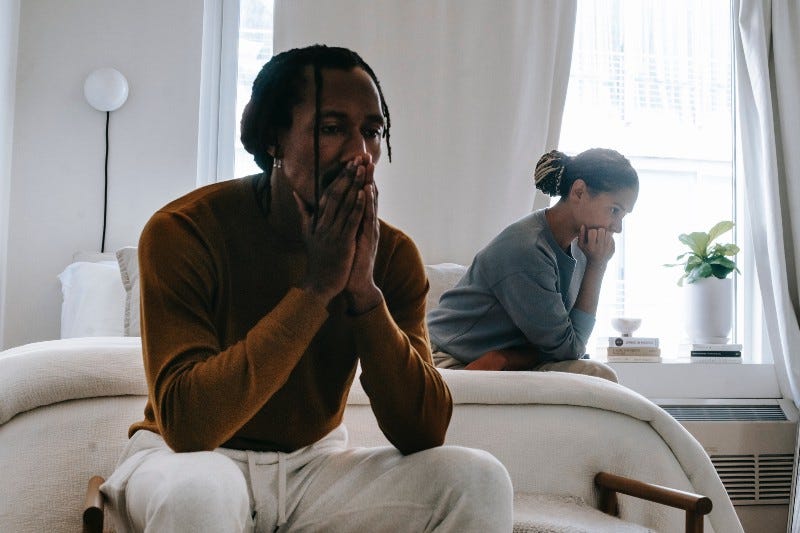 A worried couple sits on their bed, thinking hard A worried couple sits on their bed, thinking hard