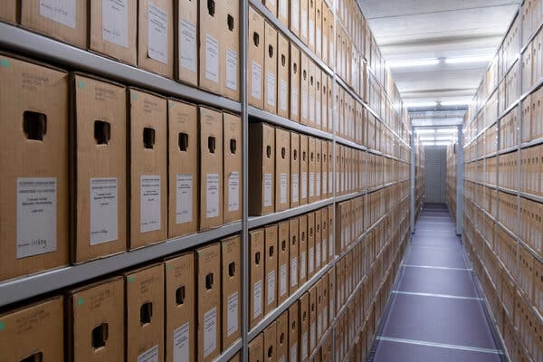 Two long rows of shelves containing file boxes separated by a walkway Two long rows of shelves containing file boxes separated by a walkway