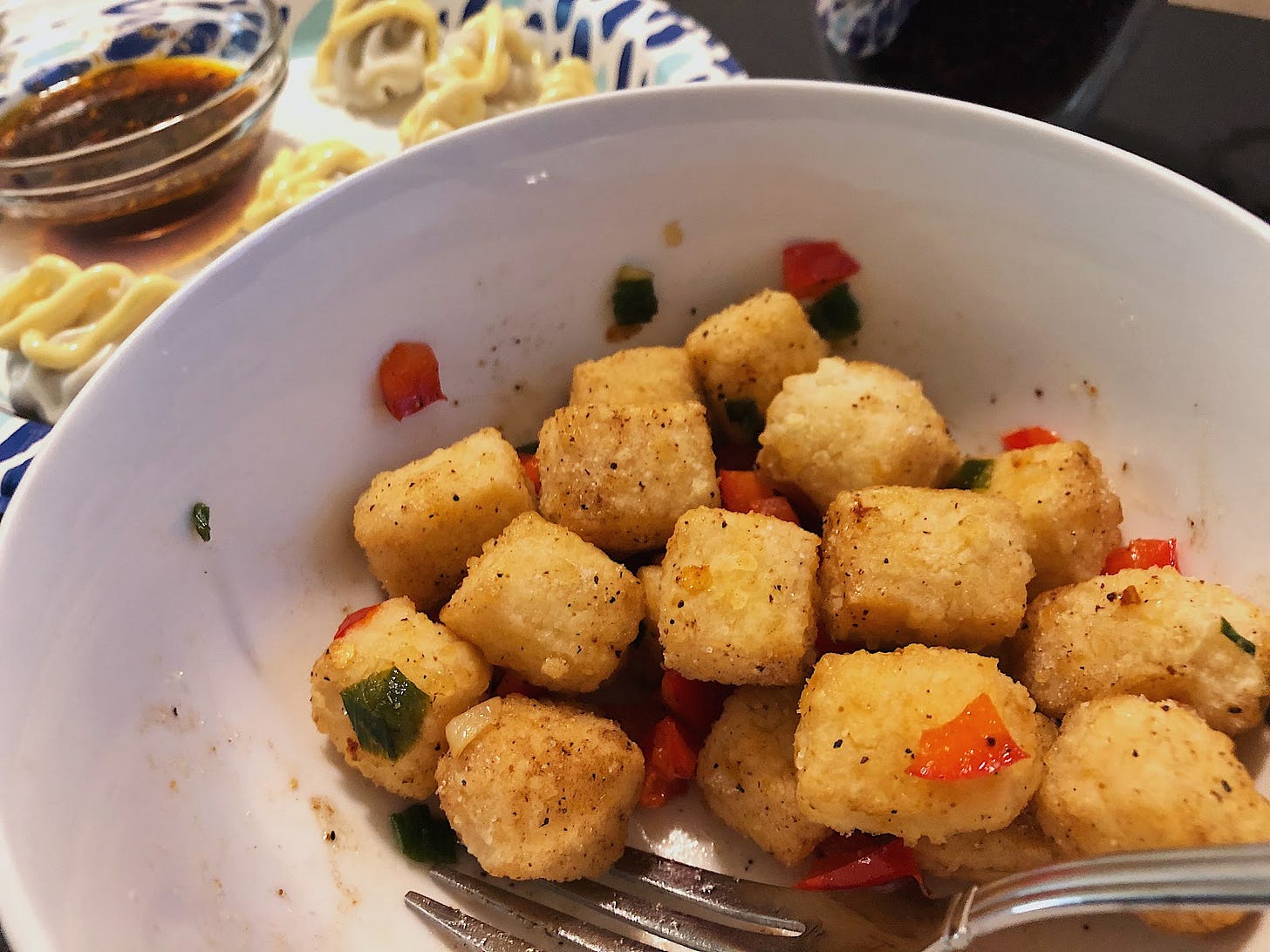 A picture of squared and salt and pepper fried tof with steamed dumplings blurred in the background covered in Japanese mayo.u
