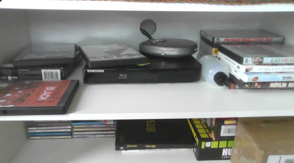 dvd player surrounded by stacks of dvds on a white shelf