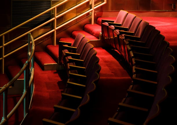 Photo of two rows of traditional red balcony theatre seats, taken from one side along the rows.