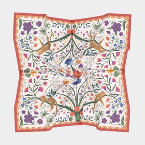 May include: A white silk scarf with a red border. The scarf features a repeating pattern of green plants, orange, pink, and purple flowers, and orange and brown leopards. The scarf is folded in the center.