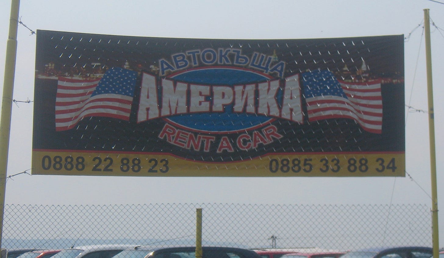A sign above a parking lot reads "AMERICA Rent a Car" in both Bulgarian and English