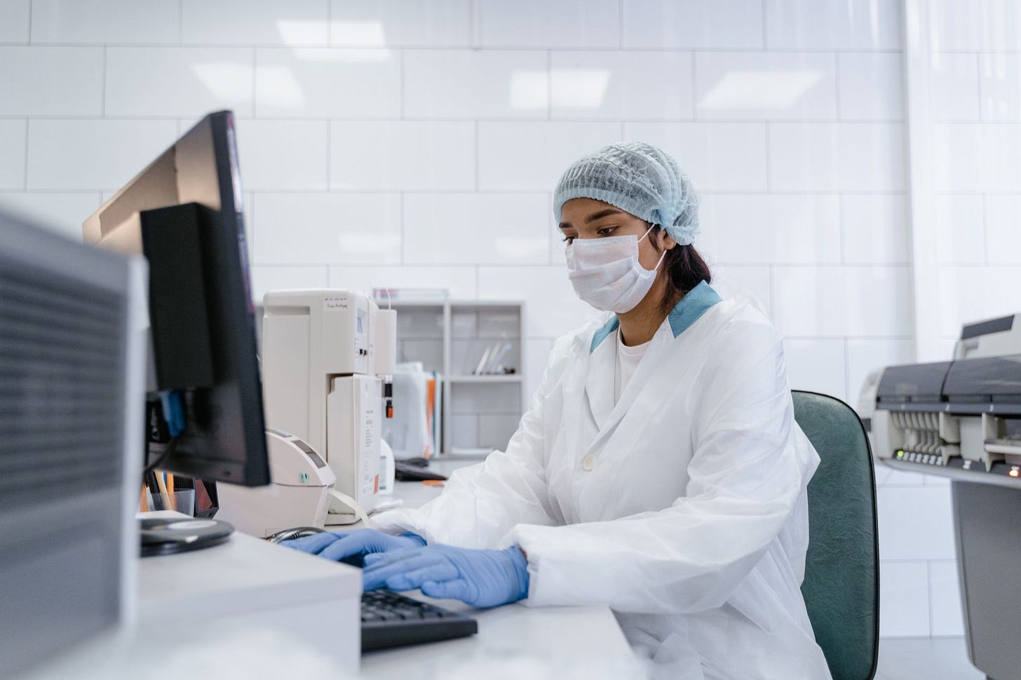 Photo by Tima Miroshnichenko on Pexels Scientist using a computer in a laboratory with protective gear including gloves, mask, and hair net. (stock photo)
