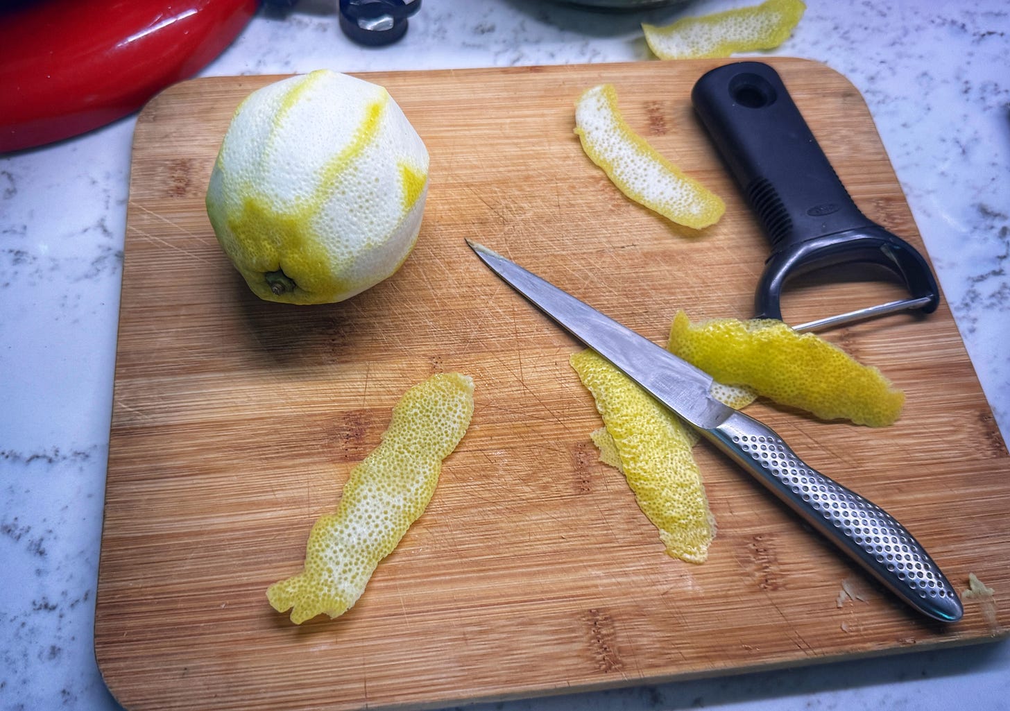 A lemon that has had all of its rind peeled from it on a cutting board. A paring knife has scraped the white pith from strips of rind. A lemon that has had all of its rind peeled from it on a cutting board. A paring knife has scraped the white pith from strips of rind.