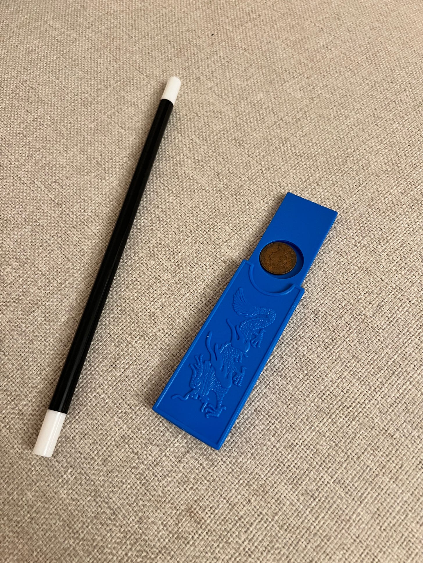 A picture of a magic wand and a small blue box used for a coin trick