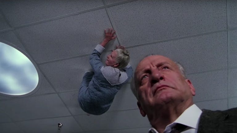 close up of george c. scott, from ground upwards. above him on ceiling an old woman is crawling
