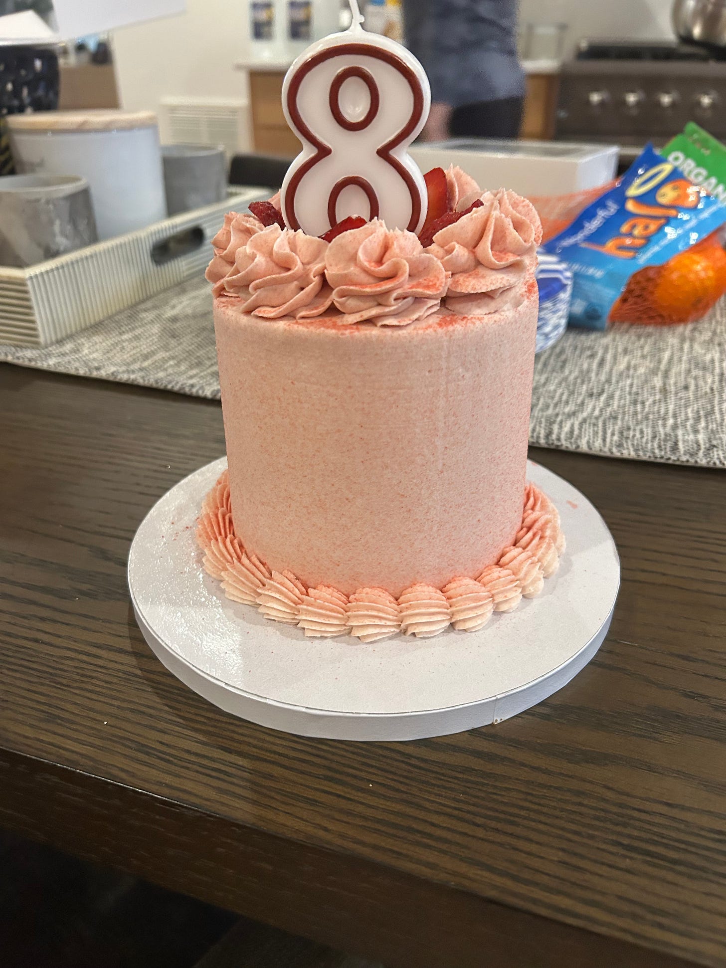 A pink strawberry layer cake with buttercream rosettes and a number eight candle on a white cake board