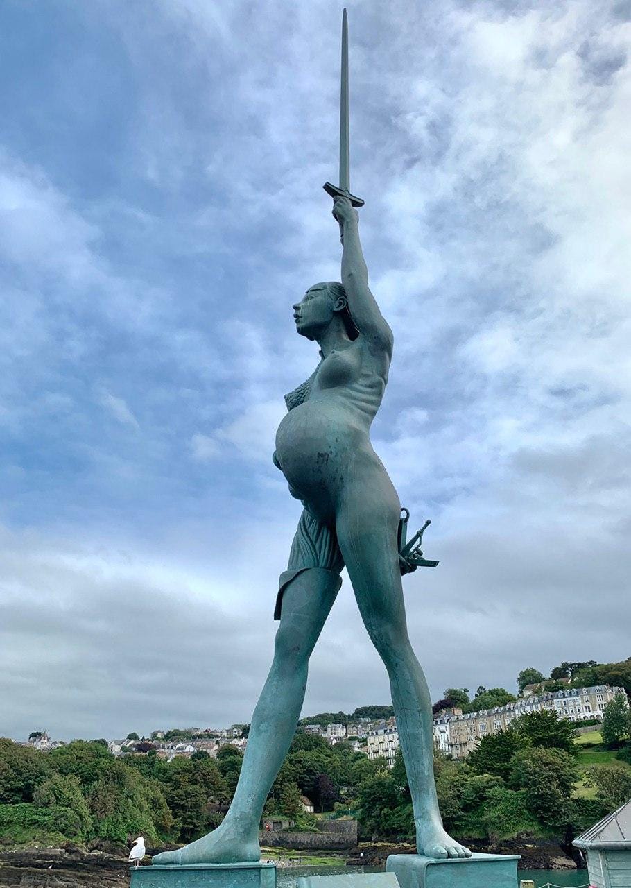 Statue of a naked pregnant woman holding a sword to the sky and scales behind her back, standing on a pile of books