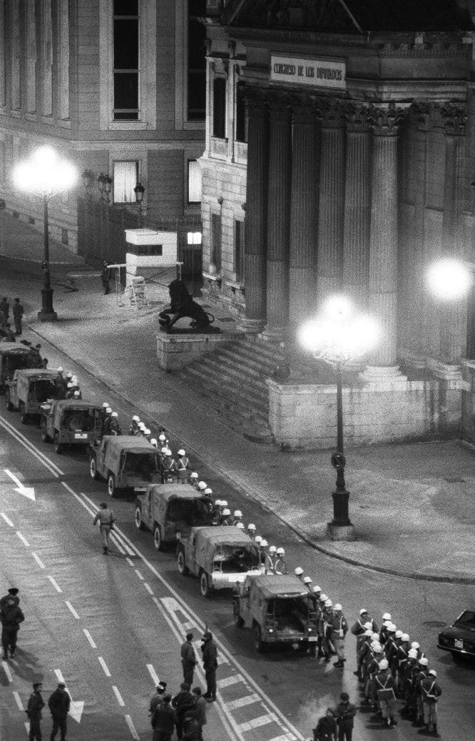 Aspecto que ofrecía el palacio del Congreso de los Diputados a las dos de la madrugada. Junto a las verjas del edificio (arriba en la foto) puede verse a tres miembros de la Guardia Civil. Alineados junto a sus vehículos, varias unidades de la Policía Militar que habían llegado con Ricardo Pardo Zancada (comandante de infantería que había intentado sin éxito que la División Acorazada Brunete se sublevara y sacar los tanques a las calles de Madrid, pero que consigue llegar al Congreso con un centenar de hombres de la Policía Militar). En primer término miembros del GEO. Hasta altas horas de la madrugada se había especulado sobre una posible intervención del Grupo Especial de Operaciones de la Policía en el rescate de los diputados. A las cinco de la madrugada, el comandante David Cervera, jefe del Estado Mayor de la Policía Nacional, negaba tal posibilidad en una rueda de prensa en el hotel Palace.