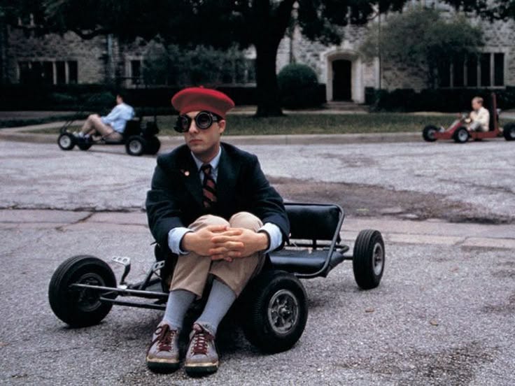 This may contain: a man in a suit and tie sitting on top of a small cart with wheels