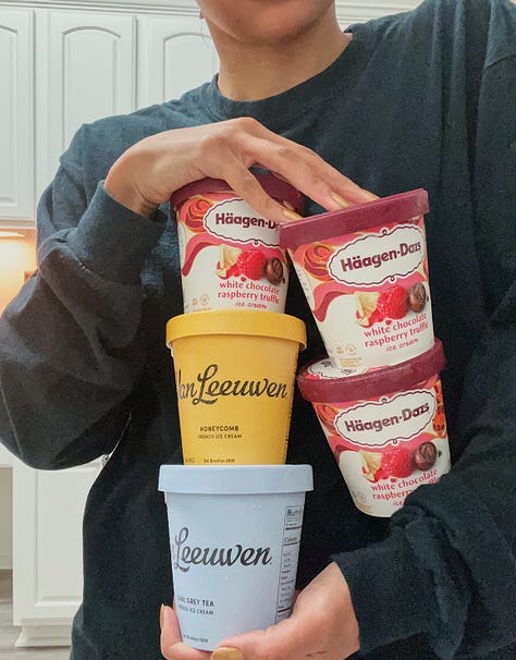 hands holding five pints of ice cream, a hand holding a perfume sample in front of a big green plant leaf, four lip products on a table in front of a sand zen garden and vase, a handful of shaved curly black hair, a hand holding a light beige mug with illustrated plants all over it, an above view of a meal on a plate with toasted english muffins, black tea, mozarella slices, and ramen
