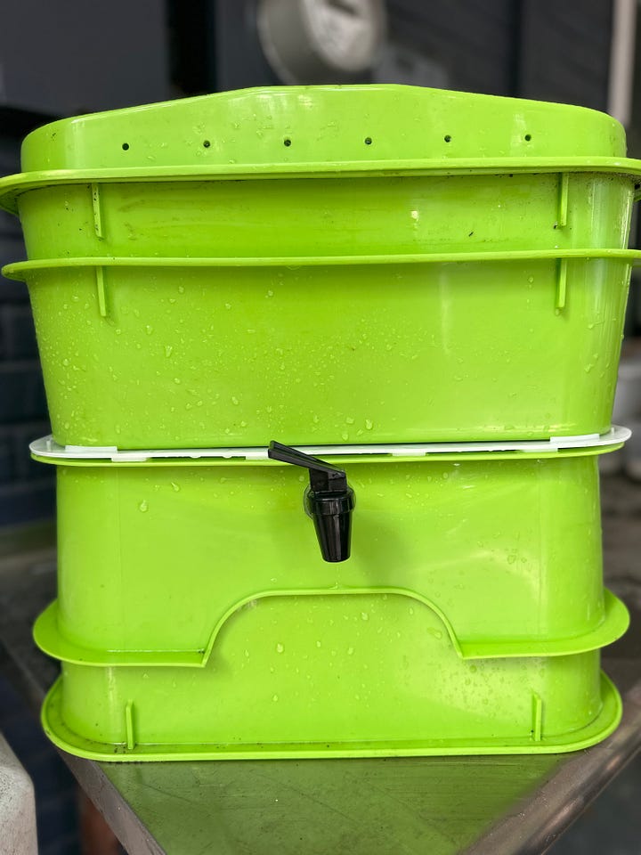 A green multi-layer vermicomposting bin with a black spout.