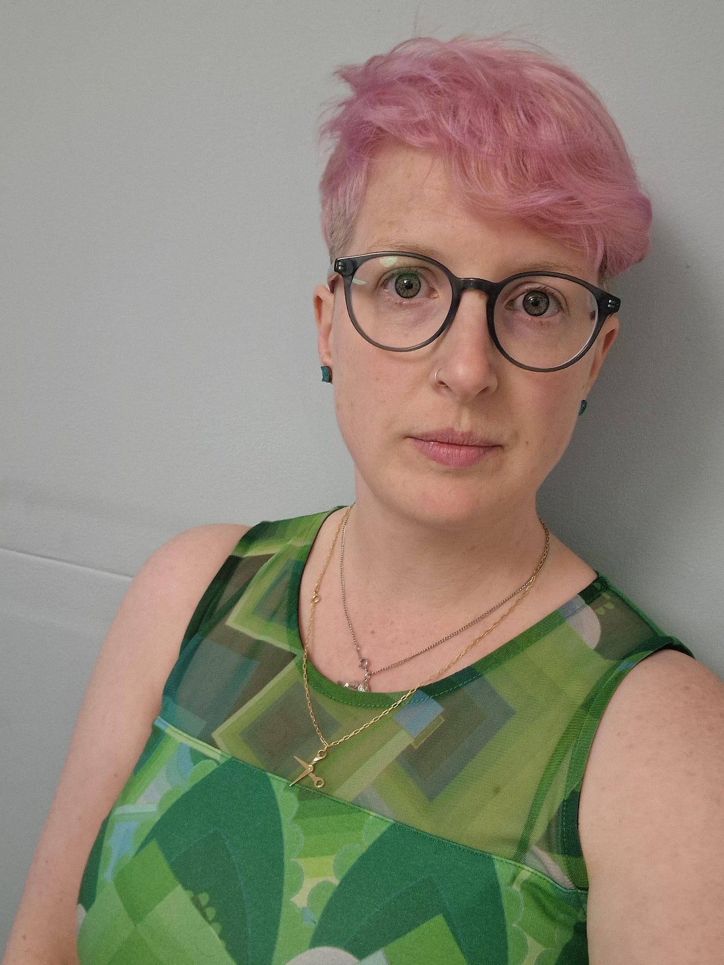 a white woman with short pink hair and black glasses looks at the camera