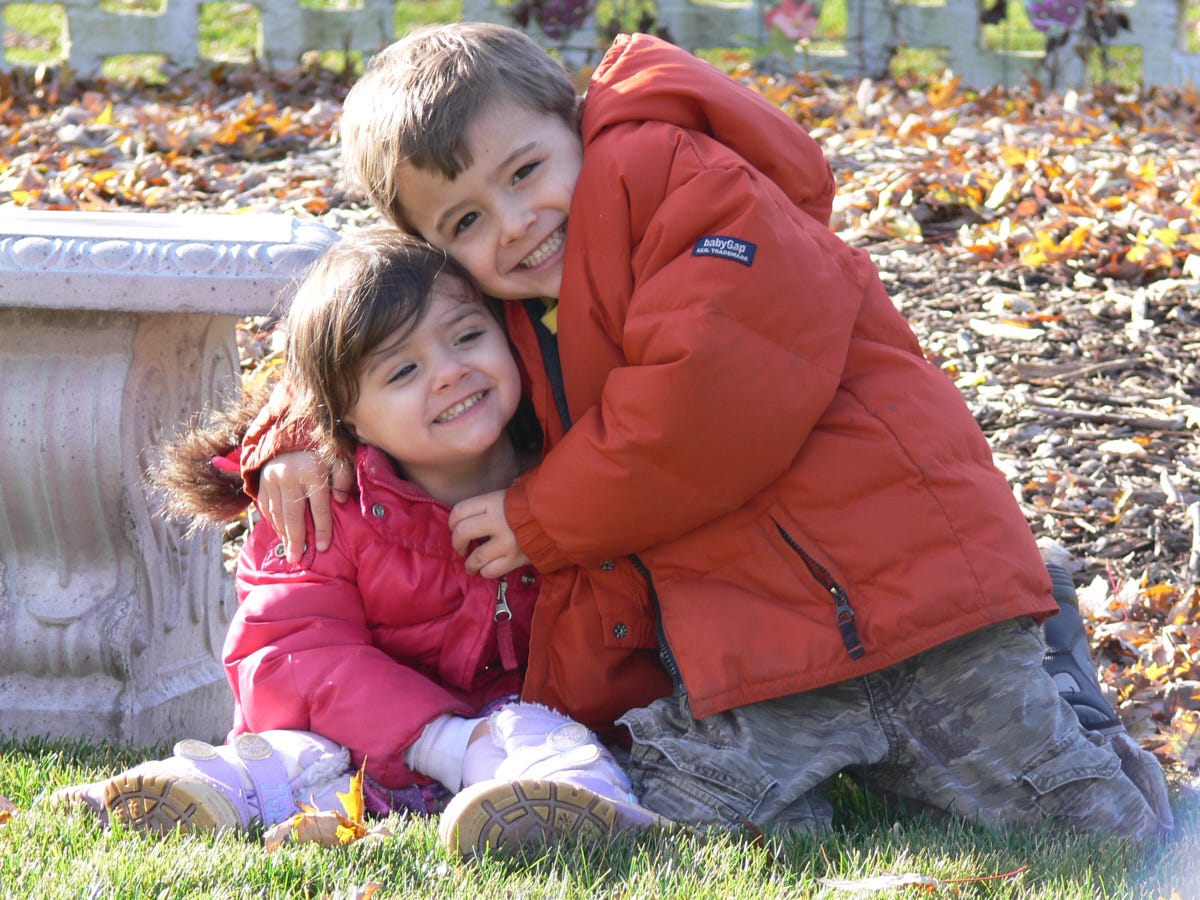 a boy and girl in a garden with fall leaves