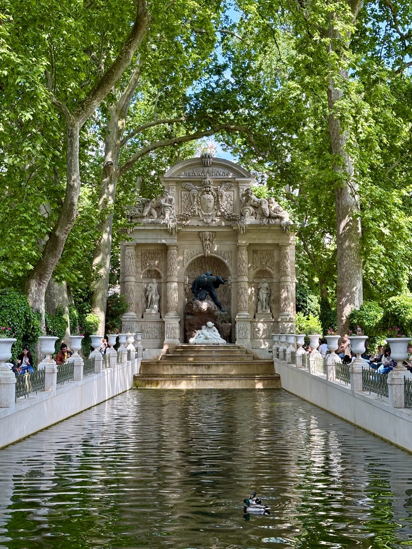 A pond with a fountain and people sitting around it

AI-generated content may be incorrect.