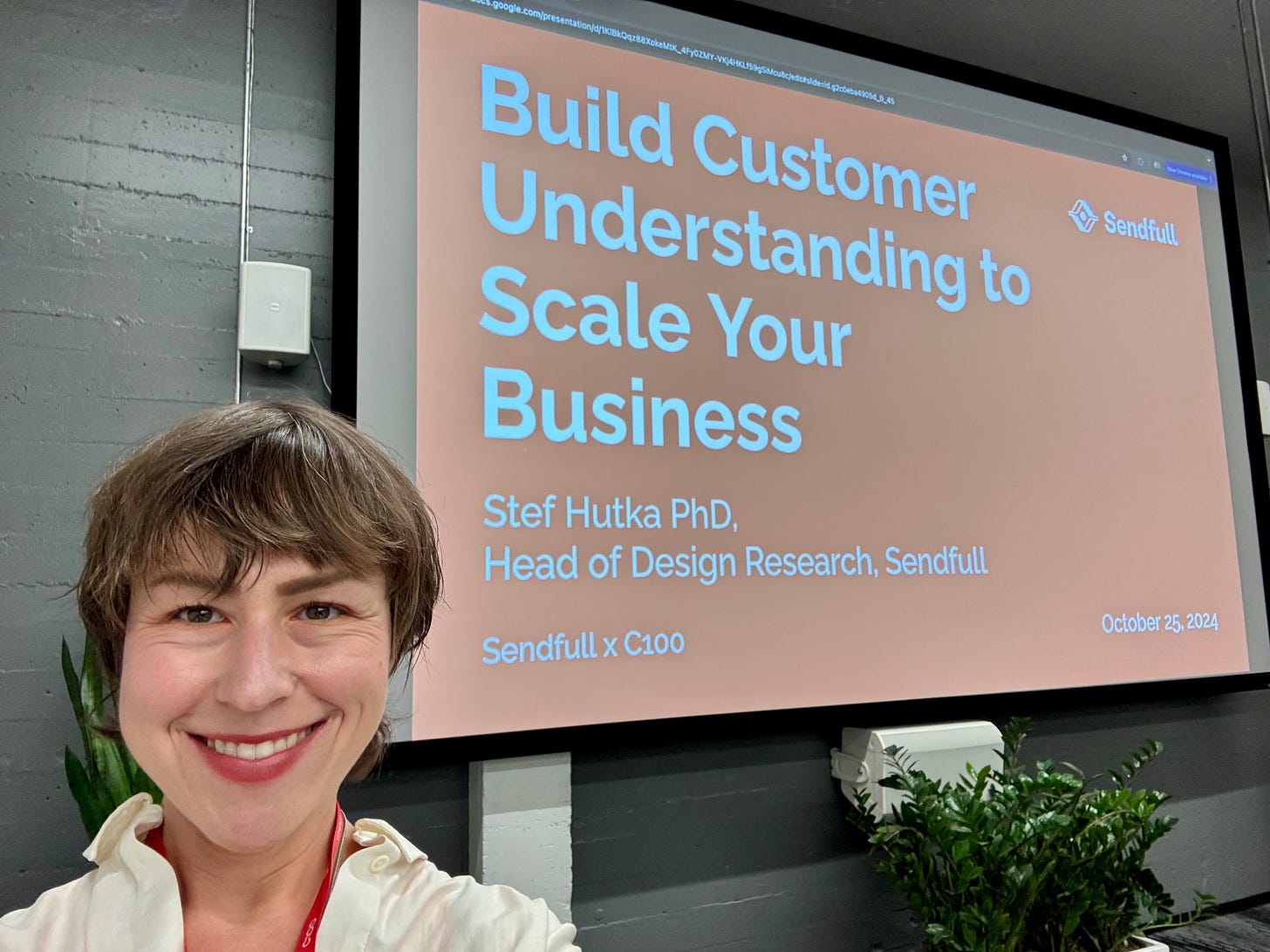 A woman with short, brown hair stands in front of a large red slide. It reads: Building Customer Understanding to Scale your Business.