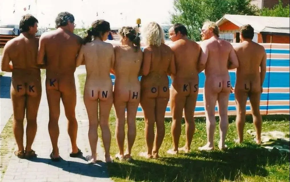 A group of nude adults stand side by side with their backs to the camera at a campsite, each with a letter painted across their lower backs spelling “FKK in Hooksiel.” A group of nude adults stand side by side with their backs to the camera at a campsite, each with a letter painted across their lower backs spelling “FKK in Hooksiel.”