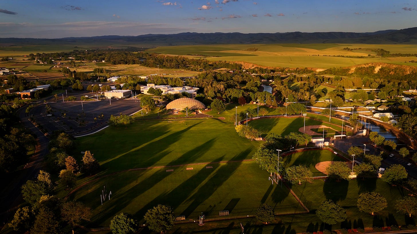 Aerial view of a green campus at sunset with mountains in the distance.