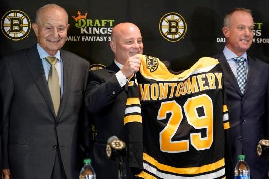 Boston Bruins newly hired head coach Jim Montgomery, center, displays a Bruins jersey while standing with team owner Jeremy Jacobs, left, and CEO Charlie Jacobs, right, during a news conference, Monday, July 11, 2022, in Boston. The Bruins hired Montgomery at the start of the 2022 season as their new coach, giving the hockey lifer another chance at an NHL head-coaching job less than three years since he lost his first one. (AP Photo/Steven Senne, File)
