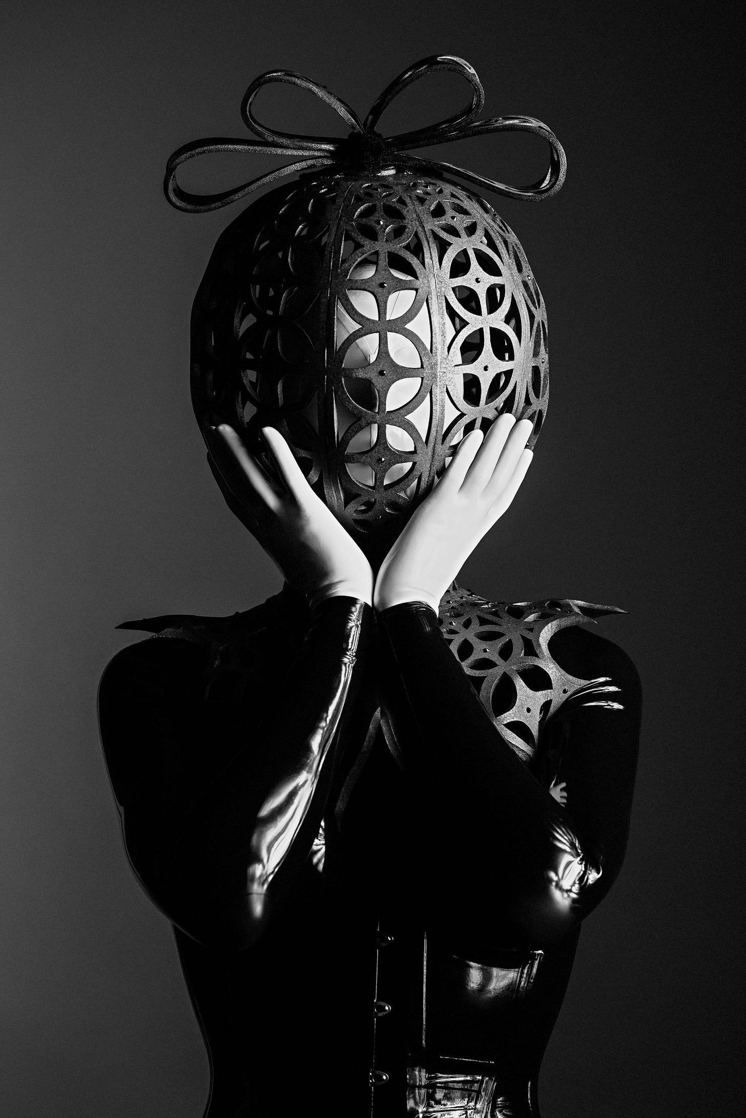 Person in black latex with white gloves wearing a metal mask with a metal bow. Bizarre, even for someone who likes bizarre fashion