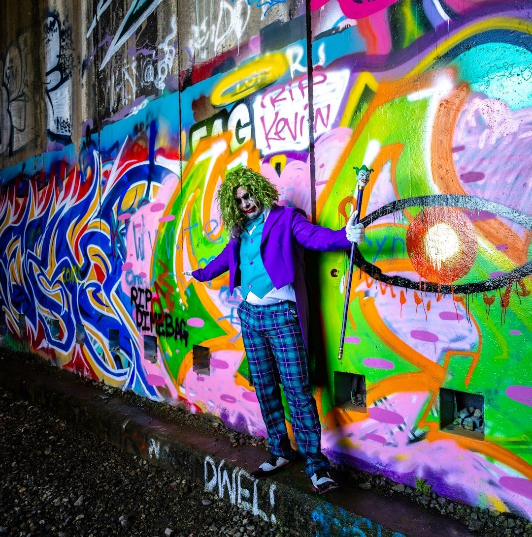 Man in joker costume stands against graffiti wall