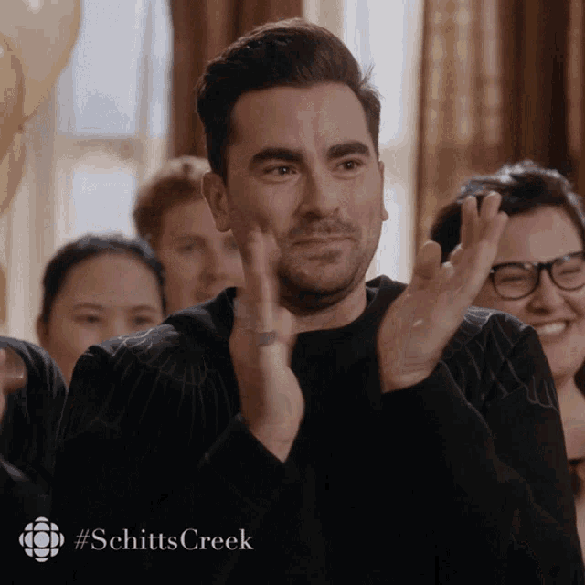 a man applauds with the #schitts creek logo behind him a man applauds with the #schitts creek logo behind him