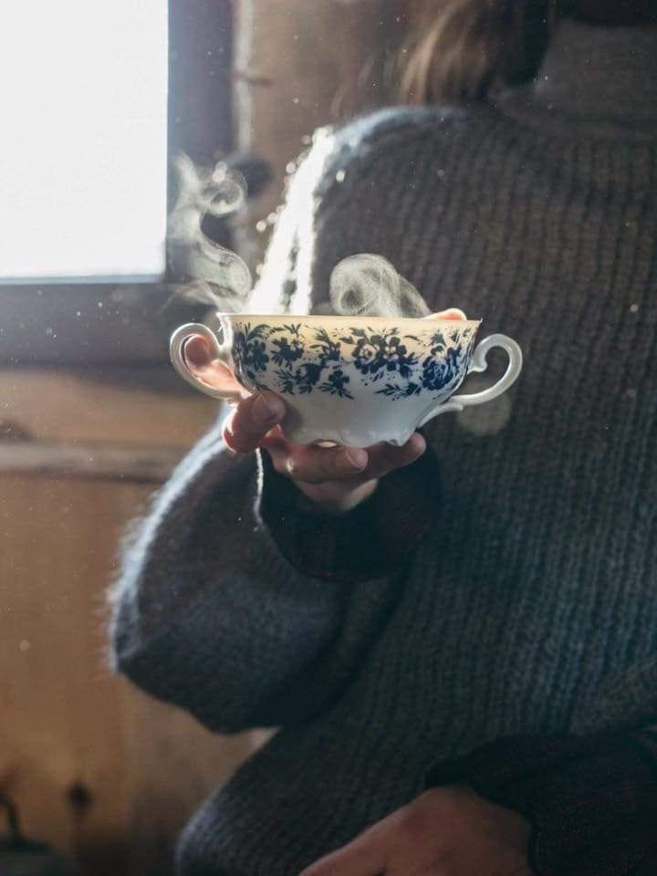 This may contain: a woman holding a cup with steam coming out of it