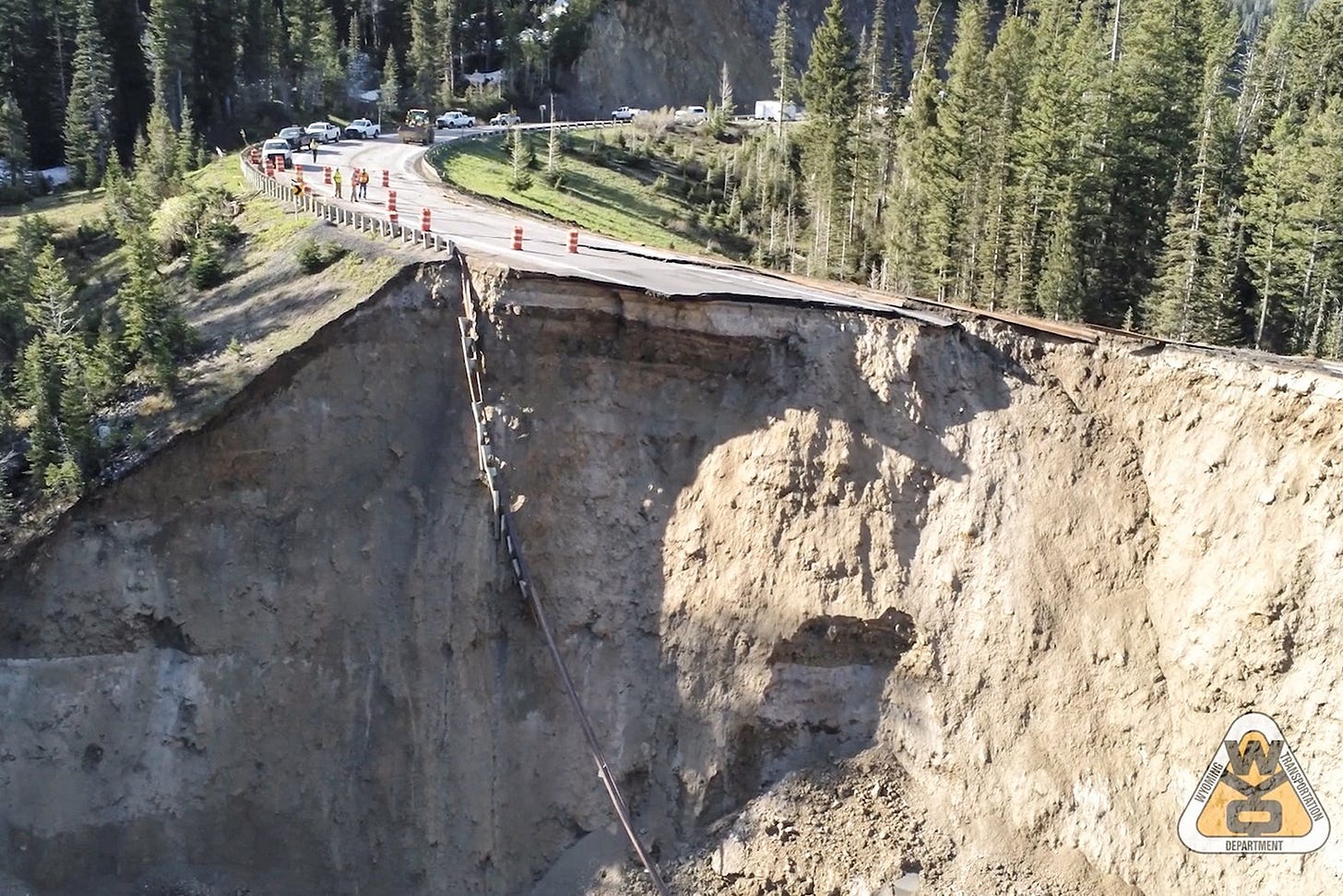 An aerial image shows a high road completely crumbled away and the guardrail dangling over the cliffside. 
