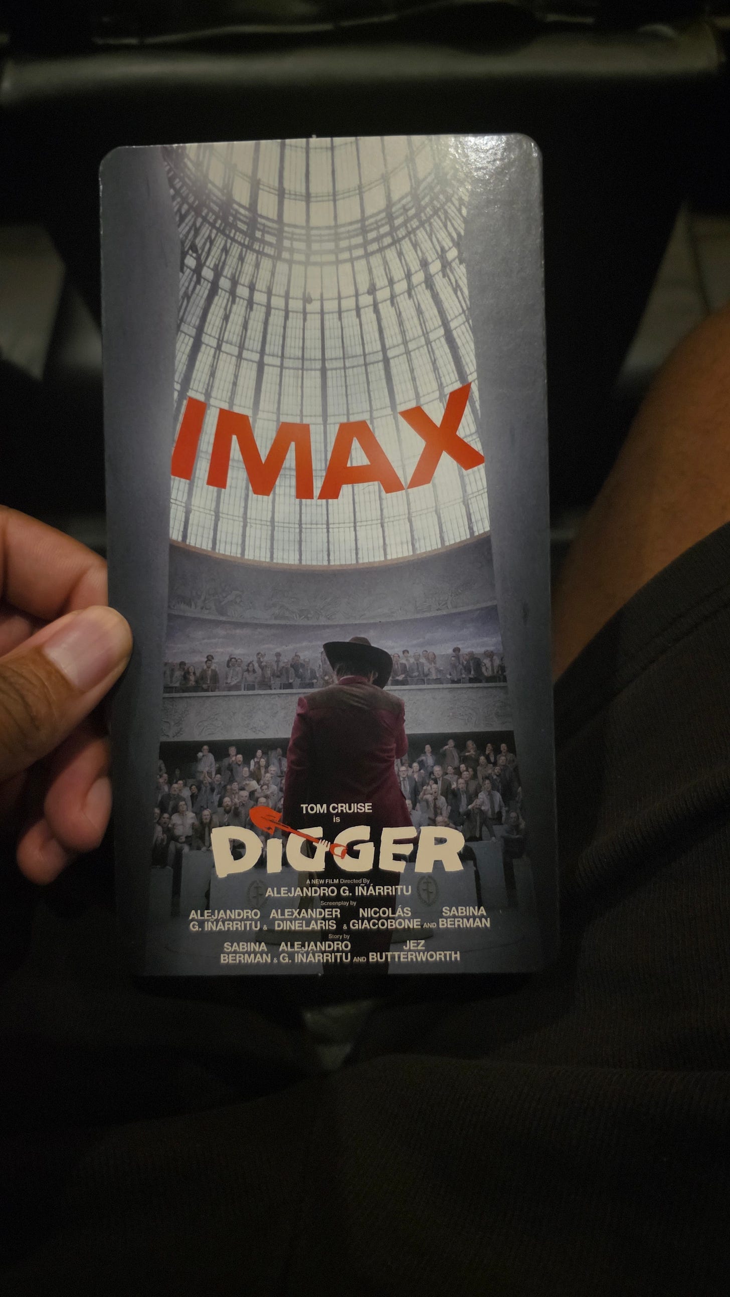 My hand holding an IMAX card for Digger, starring Tom Cruise: a man in a cowboy hat faces a packed, domed hall.