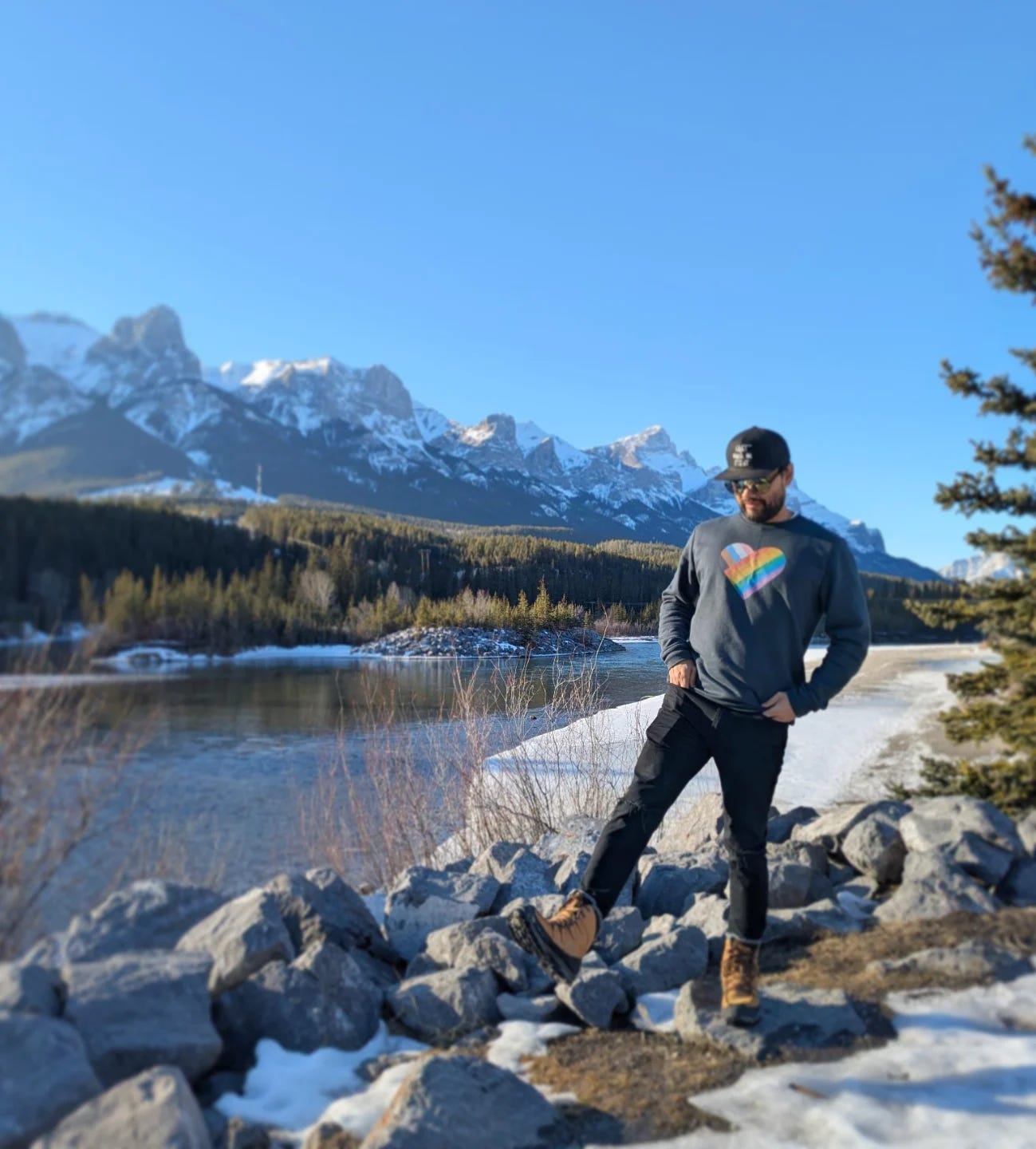 Rohadi in the foreground wearing a sweatshirt with a heart. Background is a mountain range. River running beside him. Rohadi in the foreground wearing a sweatshirt with a heart. Background is a mountain range. River running beside him.