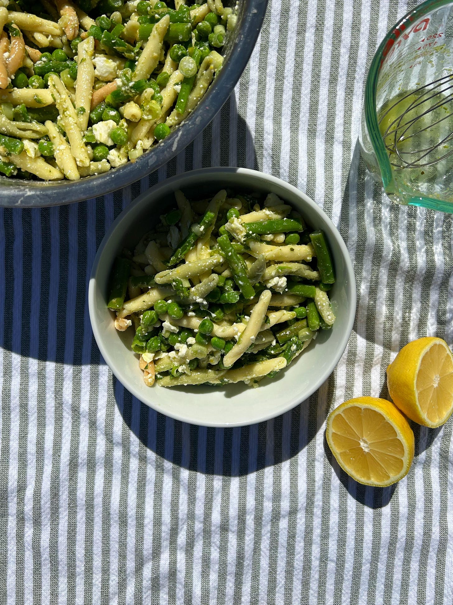 spring pasta salad in a white bowl with a striped background