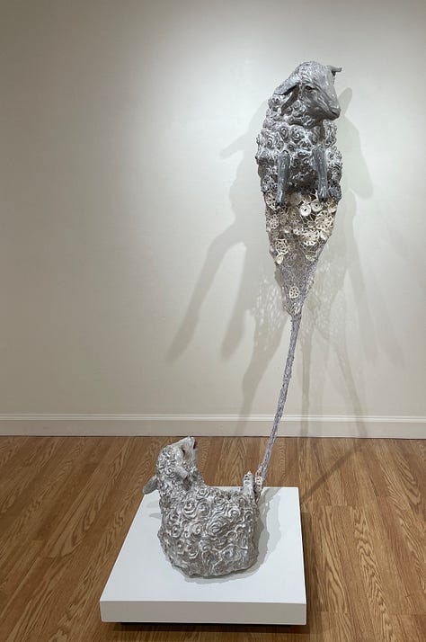 Installation views of a gallery with several artworks depicting sheep. All works are made of ceramic with fiber attachments connecting them together.