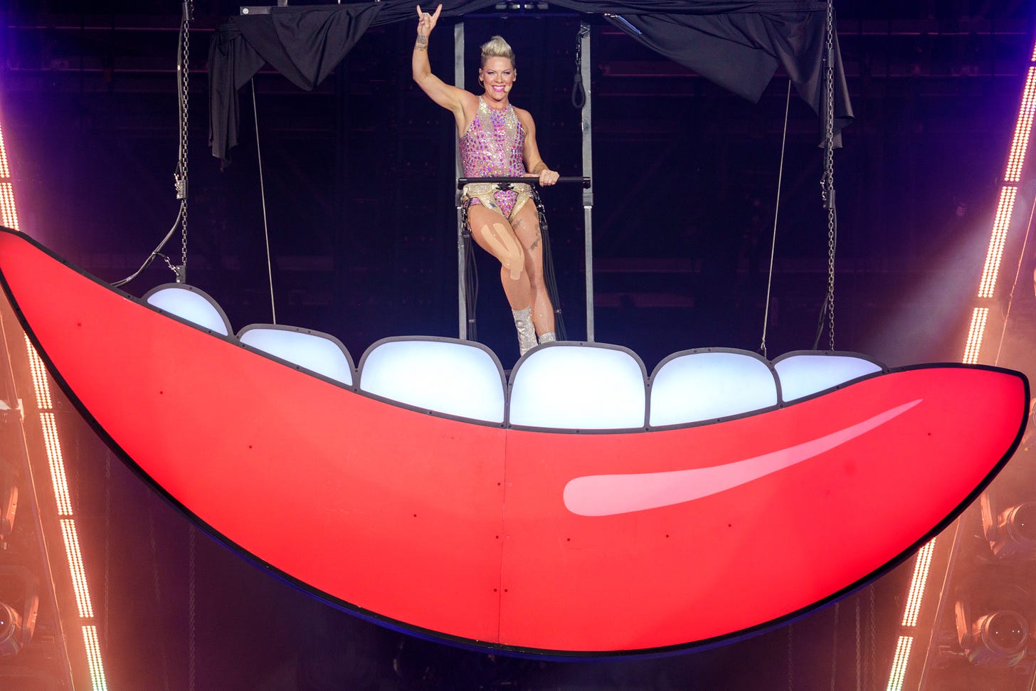 A large red mouth hanging from the top of the stage opens to reveal P!nk inside wearing a harness.