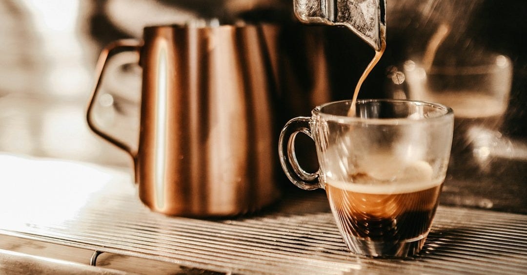 grey industrial coffee maker pouring espresso in clear glass cup
