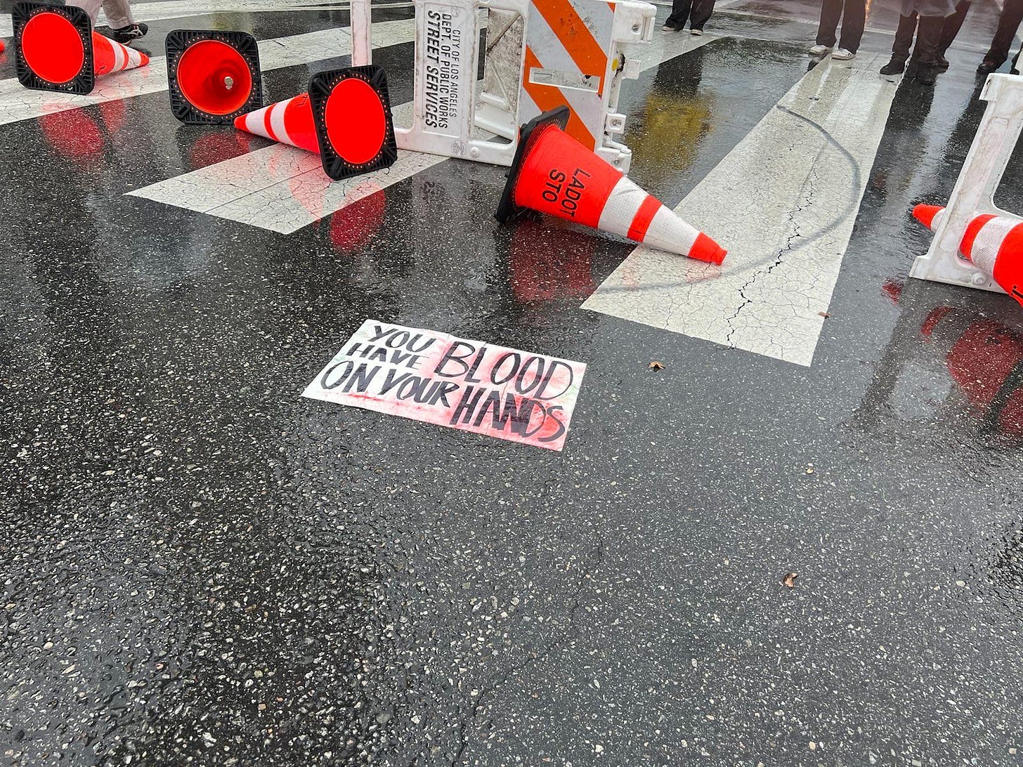 sign on street reads, "you have blood on your hands" next to barricade that has been placed by demonstrators.