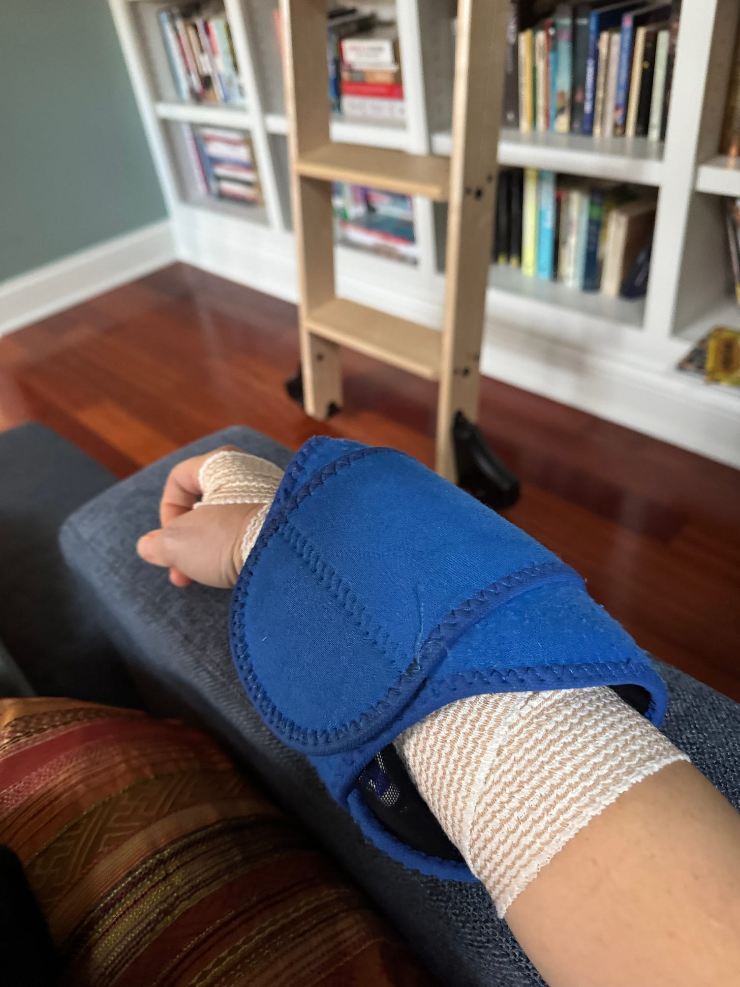 a photo of my right arm, resting on the arm of a sofa, wrapped in an ace bandage and an ice pack
