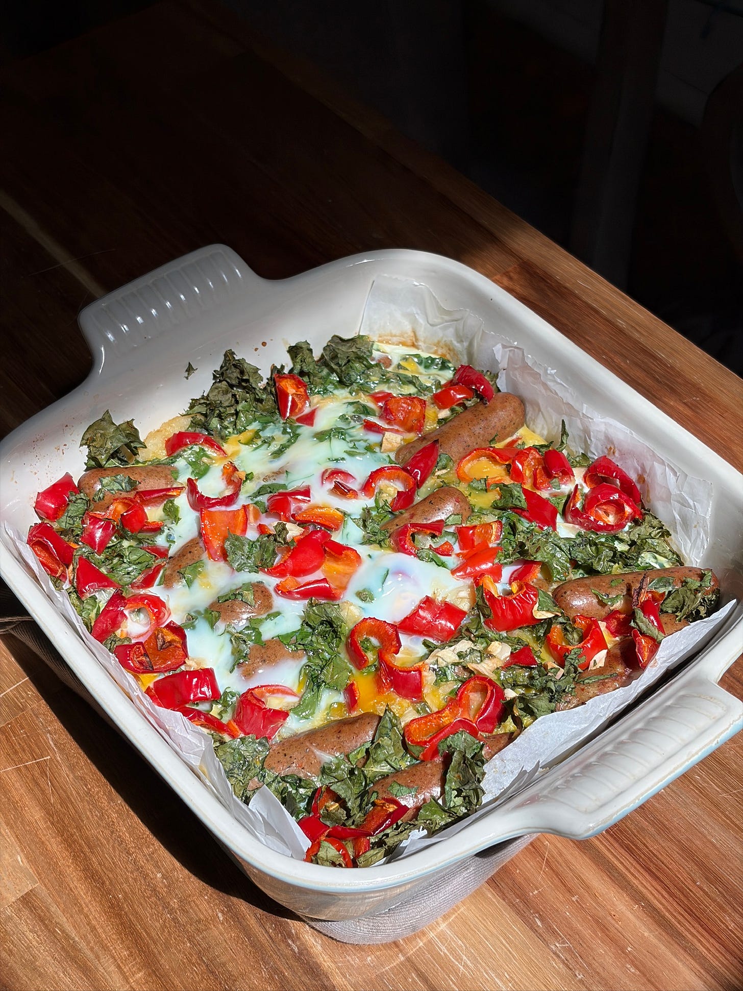 Dairy-free hashbrown breakfast casserole in a white square baking dish topped with golden eggs, kale, and red bell pepper