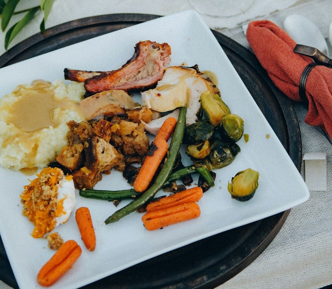 a white plate topped with meat and veggies next to a glass of wine