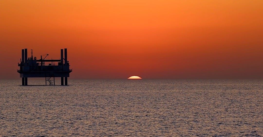 The sun is setting over the horizon of the ocean