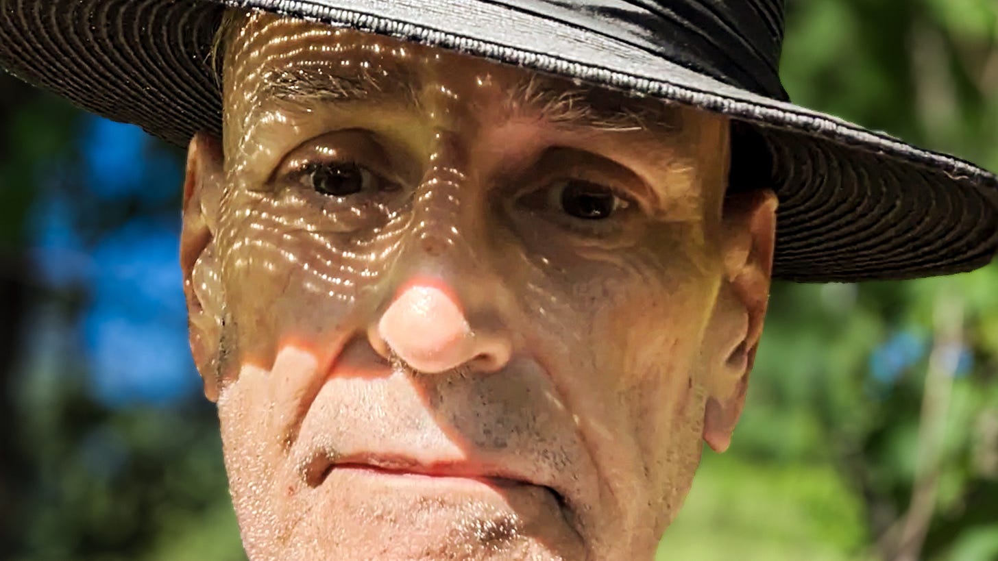High-contrast, tight close-up of Johnny Profane Âû in a black panama hat, featuring a distinct pattern of light and shadow filtering across his face.