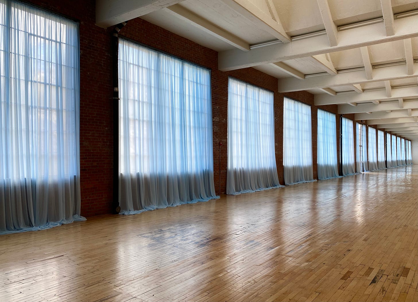 Installation view of Felix Gonzalez-Torres “Untitled” (Loverboy), 1989, at Dia Beacon. A series of sheer light-blue curtains are installed along the long outer wall of a huge industrial-scale room with a wooden floor. Installation view of Felix Gonzalez-Torres “Untitled” (Loverboy), 1989, at Dia Beacon. A series of sheer light-blue curtains are installed along the long outer wall of a huge industrial-scale room with a wooden floor.