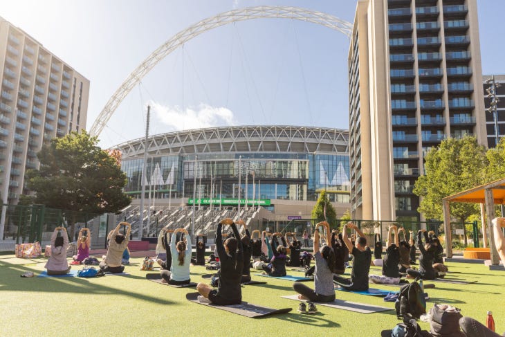Things to do in London today: people taking part in a yoga session on grass in front of Wembley Stadium Things to do in London today: people taking part in a yoga session on grass in front of Wembley Stadium