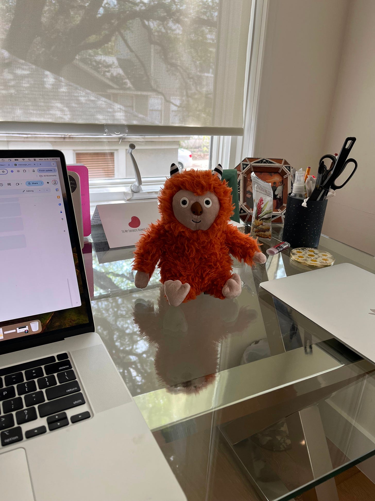A photo of a stuffed orange monster toy next to a laptop on a desk